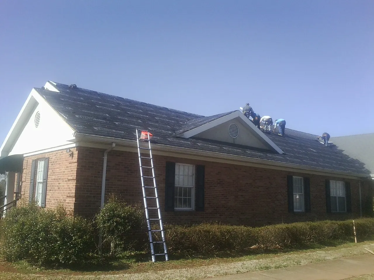Crew tearing shingles off a brick ranch roof with a ladder set — Emergency Roof Repair work by our crew in Cobb Island