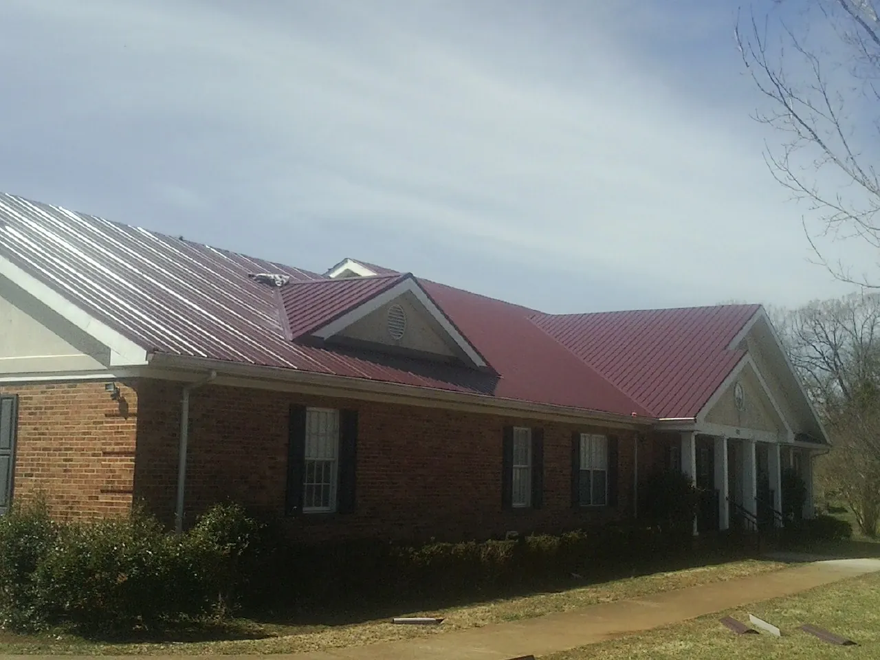 Red metal roof with gabled entries on a long brick building, from a Hail Damage Roof Repair job in Cobb Island