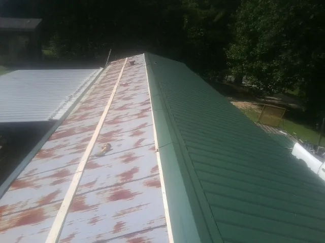 Old rusted panels beside newly installed green metal roofing — Wind Damage Roof Repair by Roofing Brothers in Cobb Island