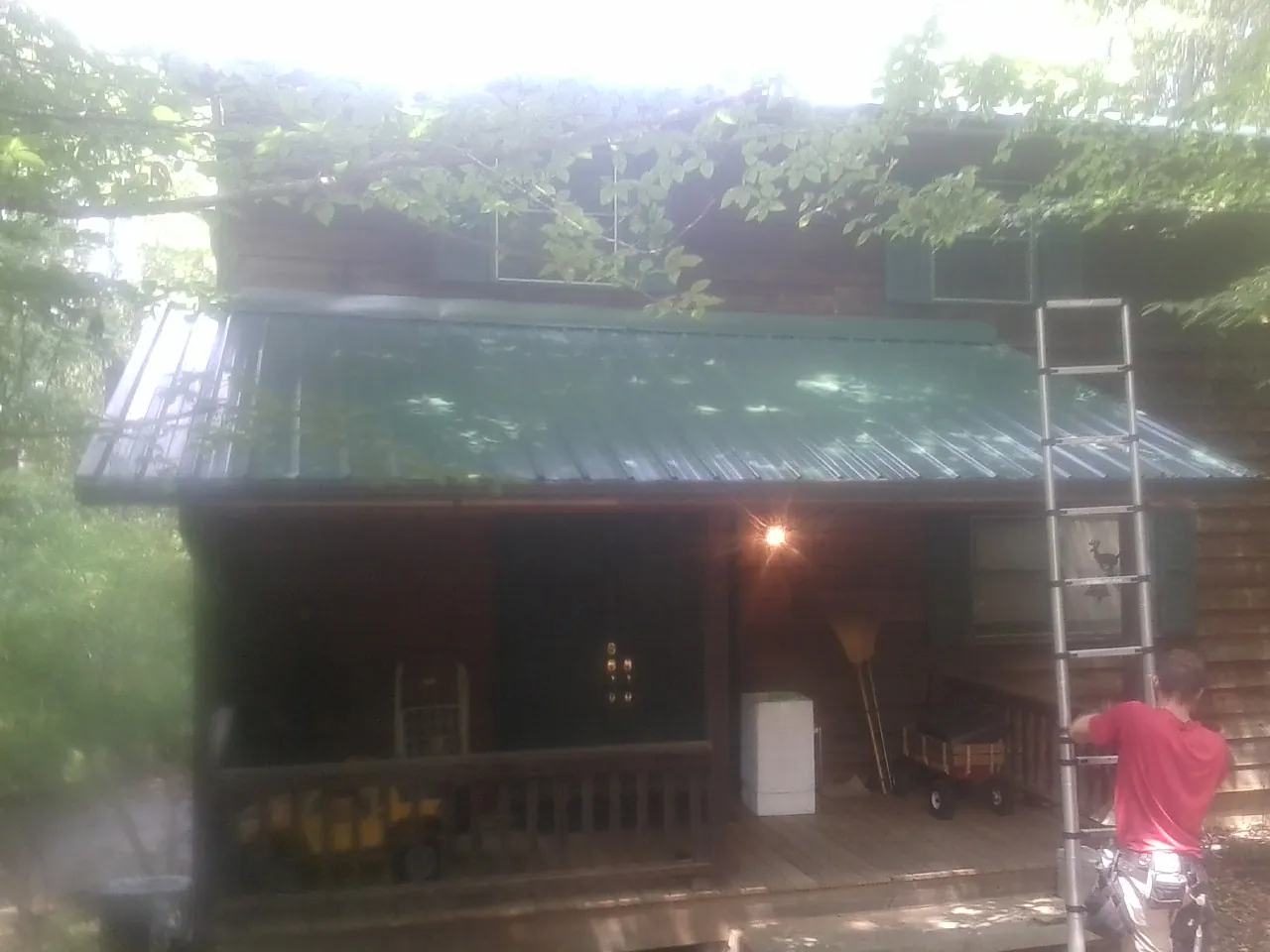 Worker on a ladder at the green porch roof of a wooded cabin in Cobb Island