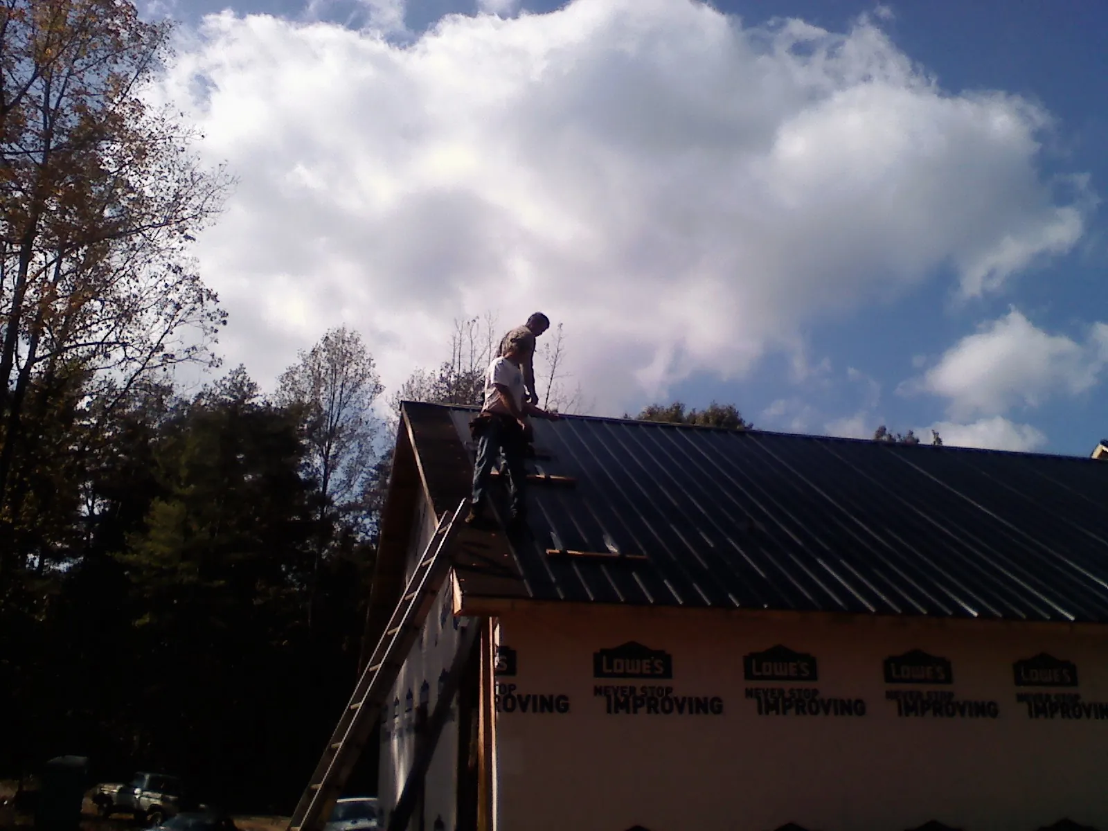 Roofer fastening dark metal panels high against a cloudy sky, from a Roof Inspection job in Cobb Island