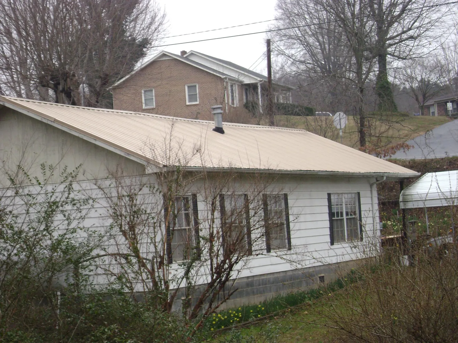 Tan metal roof on a white sided house set into a hillside — Commercial Roofing by Roofing Brothers in Cobb Island